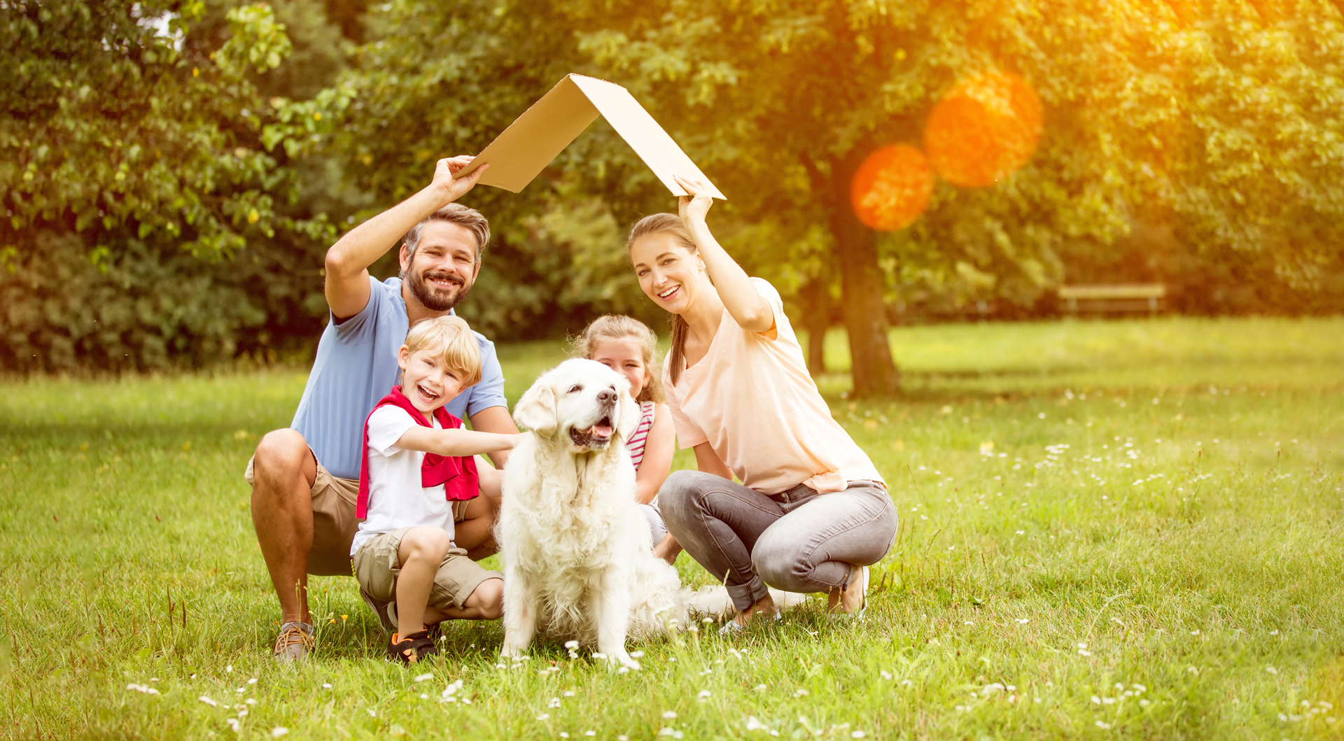 family and dog under a cardboard roof smiling in the park