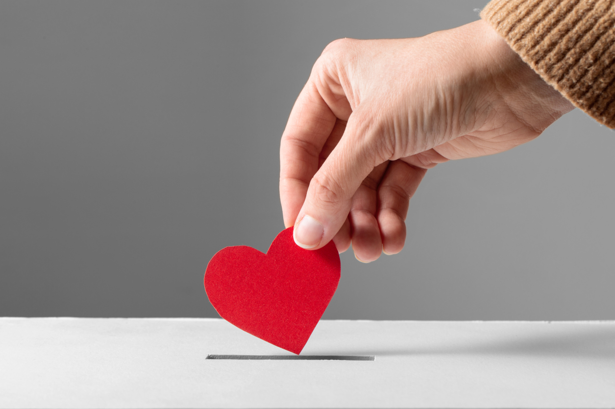 hand putting red heart into donation box